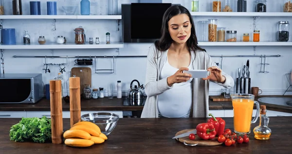 Беременная женщина фотографирует свежие продукты на кухне — стоковое фото