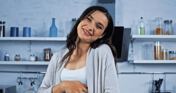 Lächelnde brünette Frau schaut in die Kamera in der Küche — Stockfoto