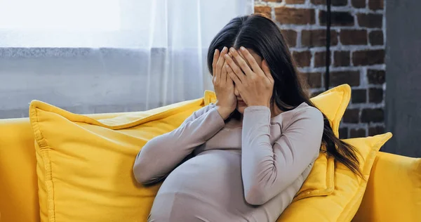 Mujer embarazada cubriendo la cara con las manos en casa — Stock Photo