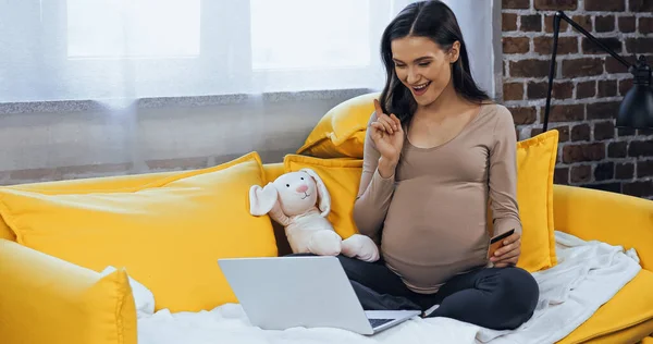 Mulher grávida sorridente com cartão de crédito olhando para laptop — Fotografia de Stock