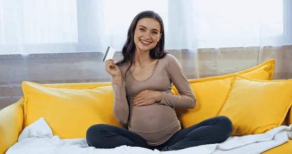 Cheerful pregnant woman holding credit card on couch — Stock Photo