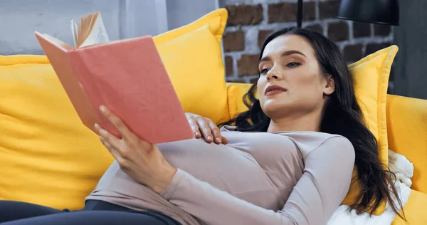 Молода вагітна жінка читає книгу, лежачи на дивані — стокове фото