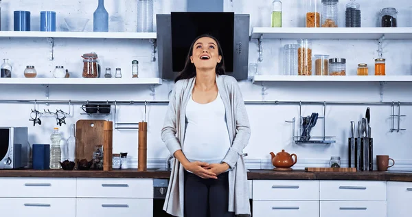 Excited pregnant woman embracing belly in kitchen — Stock Photo