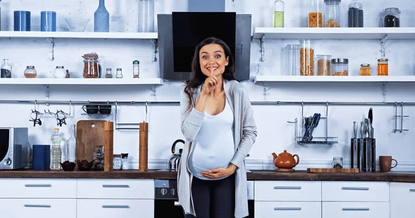 Mulher grávida mostrando gesto secreto na cozinha — Fotografia de Stock