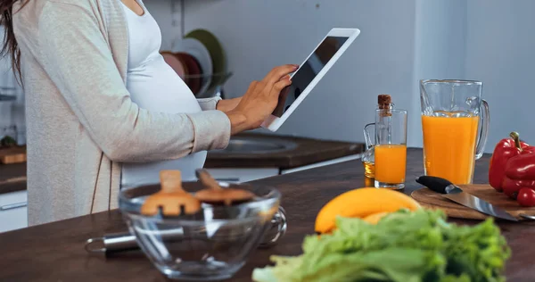 Ausgeschnittene Ansicht von Schwangeren mit digitalem Tablet in der Nähe von Lebensmitteln, Öl und Orangensaft — Stockfoto