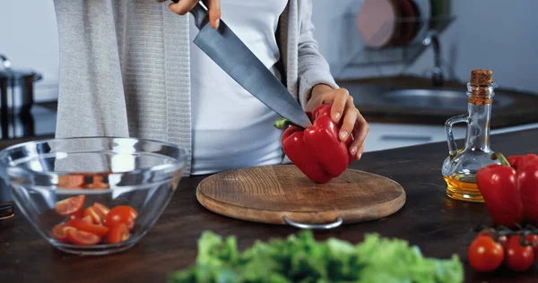 Cropped view of woman holding knife and bell pepper near vegetables on blurred foreground — Stock Photo