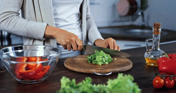 Cropped view of woman cutting lettuce near bowl and vegetables on blurred foreground — Stock Photo