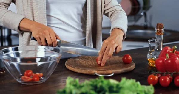 Ausgeschnittene Ansicht einer Frau, die Kirschtomaten in der Nähe von Gemüse und Salat schneidet, auf verschwommenem Vordergrund — Stockfoto