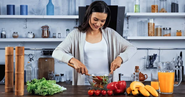 Mulher sorridente misturando salada perto de ingredientes frescos — Fotografia de Stock