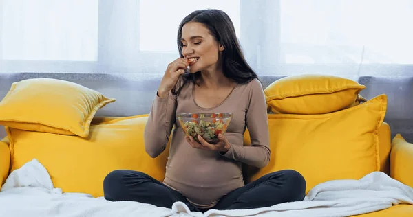 Беременная женщина ест свежий салат на диване — стоковое фото