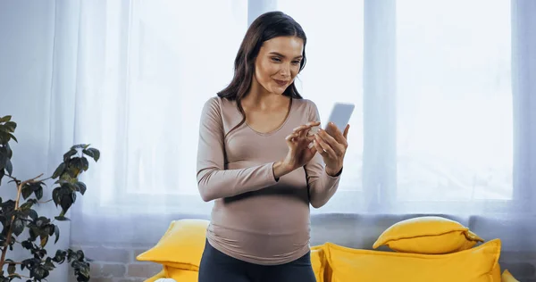 Pregnant woman using smartphone in living room — Stock Photo