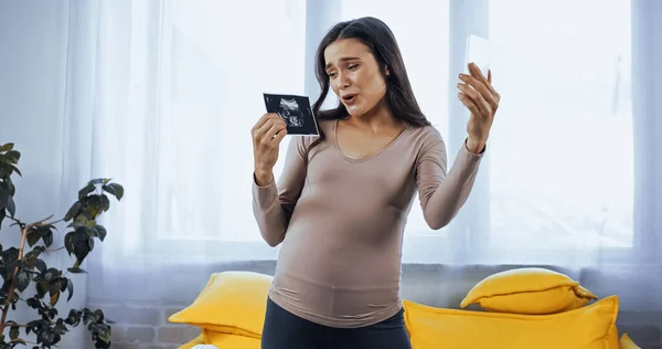 Чувствительная беременная женщина проводит ультразвуковое сканирование ребенка во время видеозвонка на смартфон — стоковое фото