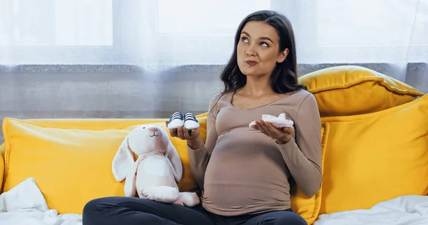 Pensive pregnant woman holding baby booties near soft toy — Stock Photo