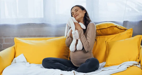 Счастливая беременная женщина обнимает мягкую игрушку в гостиной — стоковое фото