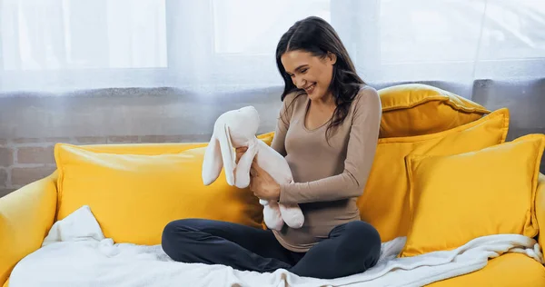 Веселая беременная женщина держит мягкую игрушку в гостиной — стоковое фото