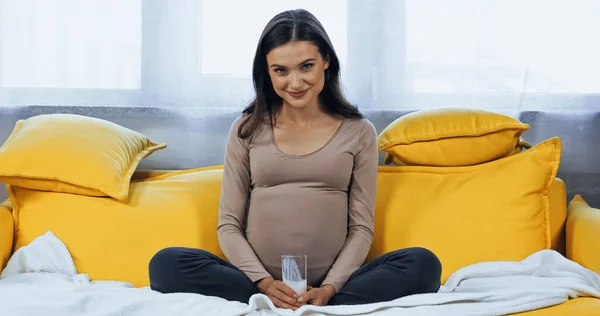 Schwangere lächelt in die Kamera, während sie zu Hause ein Glas Milch hält — Stockfoto