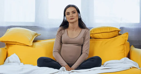 Young pregnant woman listening music in headphones on couch — Stock Photo