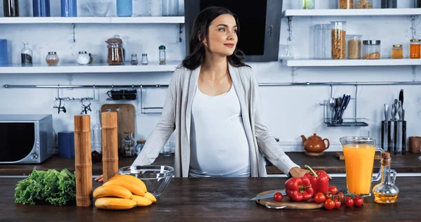 Беременная женщина стоит рядом с органической едой и апельсиновым соком на кухонном столе — стоковое фото