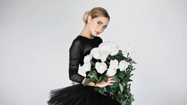 Smiling ballerina in tutu skirt holding bouquet of flowers on grey — Stock Photo