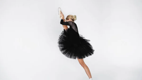 Flexible ballerina in tutu skirt and pointe shoes stretching on white background — Stock Photo