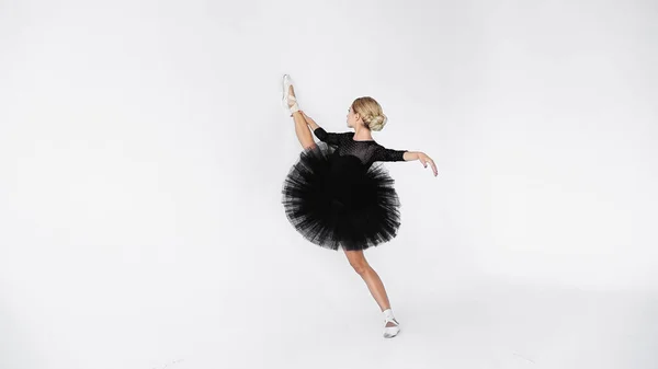 Bailarina flexible en falda de tutú y zapatos puntiagudos estirándose mientras baila sobre fondo blanco - foto de stock