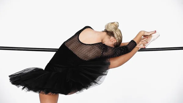 Vista trasera de la elegante bailarina practicando movimientos de ballet en barra sobre fondo blanco - foto de stock