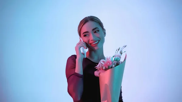 Glückliche Ballerina hält Blumen in der Hand, während sie auf dem Smartphone über blau und rosa spricht — Stockfoto