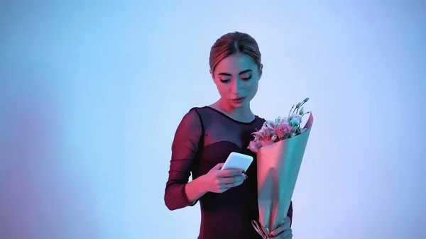 Bailarina segurando flores ao usar o smartphone no azul — Fotografia de Stock