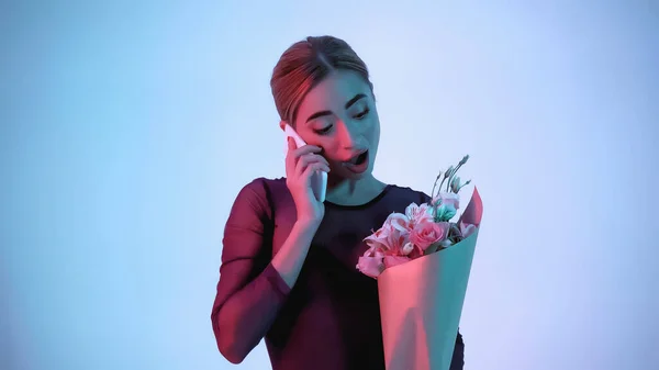 Bailarina sosteniendo flores mientras habla en el teléfono inteligente en azul - foto de stock