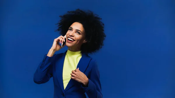 Alegre mujer afroamericana hablando en teléfono inteligente aislado en azul - foto de stock