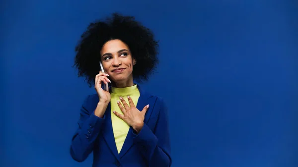Alegre mujer afroamericana hablando por teléfono celular aislado en azul - foto de stock