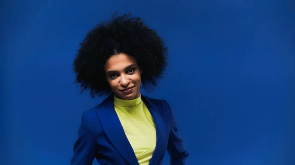 African american woman in yellow turtleneck smiling at camera isolated on blue — Stock Photo