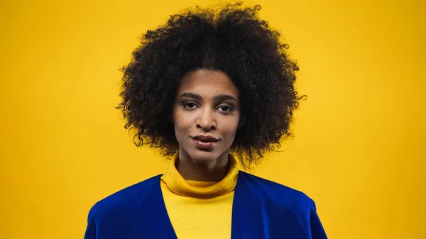 African american woman in blue jacket looking at camera isolated on yellow — Stock Photo