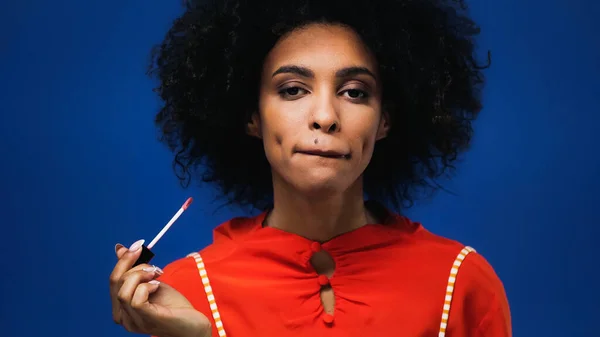 African american woman holding lip gloss isolated on blue — Stock Photo