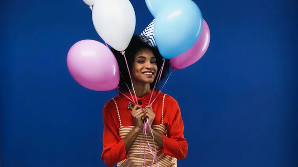 Sorrindo afro-americana segurando balões isolados em azul — Fotografia de Stock