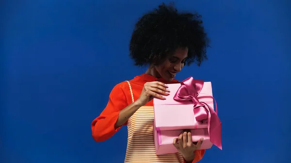 African american woman opening present isolated on blue — Stock Photo