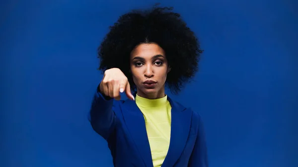 Jovem afro-americana apontando com o dedo para a câmera em primeiro plano borrado isolado em azul — Fotografia de Stock