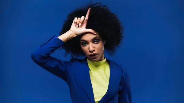 African american woman showing loser sign isolated on blue — Stock Photo