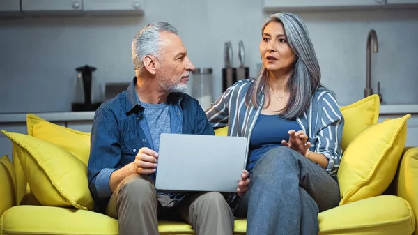 Excited asian woman talking to husband while sitting near laptop — Stock Photo