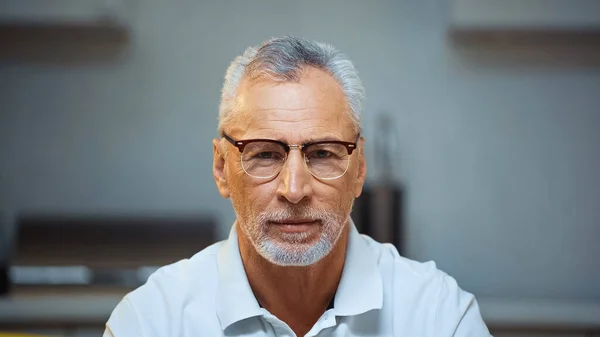 Hombre anciano positivo en anteojos mirando a la cámara en casa - foto de stock