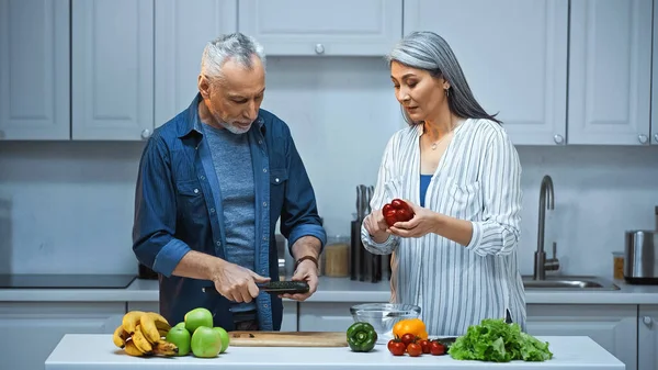 Senior interracial couple cutting fresh vegetables in kitchen — Stock Photo