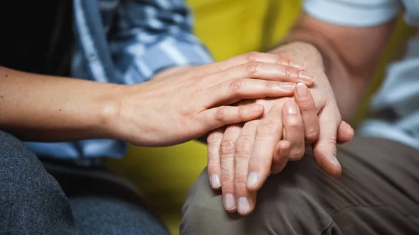 Cropped view of woman touching hand on senior husband, blurred background — Stock Photo