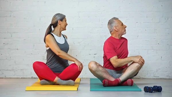 Sportif senior interracial couple méditant sur tapis de fitness en pose de lotus — Photo de stock