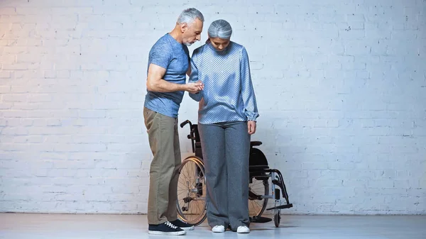 Senior man supporting handicapped asian wife near wheelchair — Stock Photo