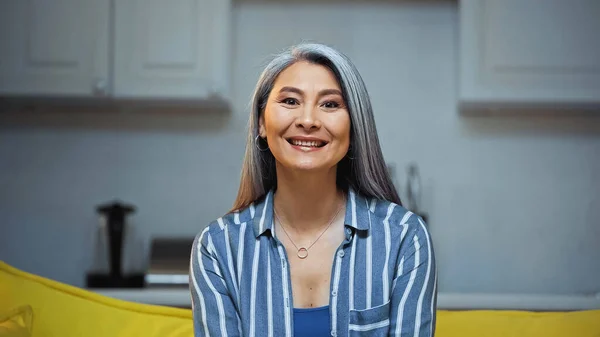 Heureux senior asiatique femme dans rayé chemise sourire à caméra à la maison — Photo de stock