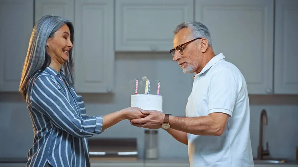 Side view of excited asian woman giving birthday cake to senior husband — Stock Photo