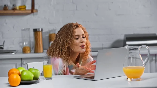 Curly young woman gesturing during video call in kitchen — Stock Photo