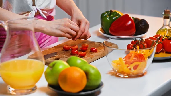 Обрезанный вид женщины возле помидоров черри и других овощей на кухонном столе — стоковое фото