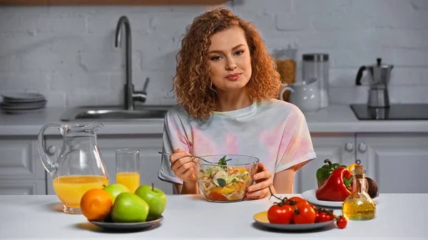 Cheerful woman holding fork near fresh salad in bowl — Stock Photo