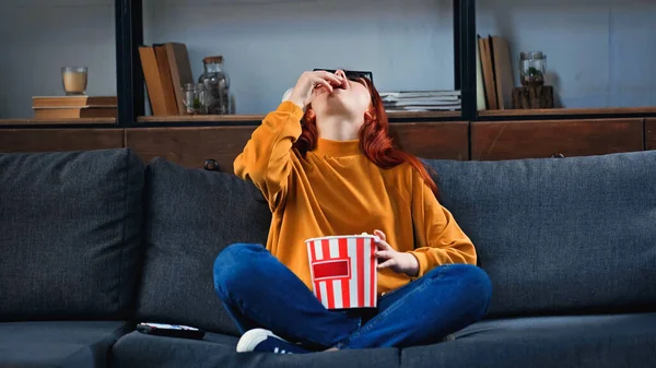 Chica en gafas 3d comer palomitas de maíz cerca de mando a distancia en el sofá - foto de stock